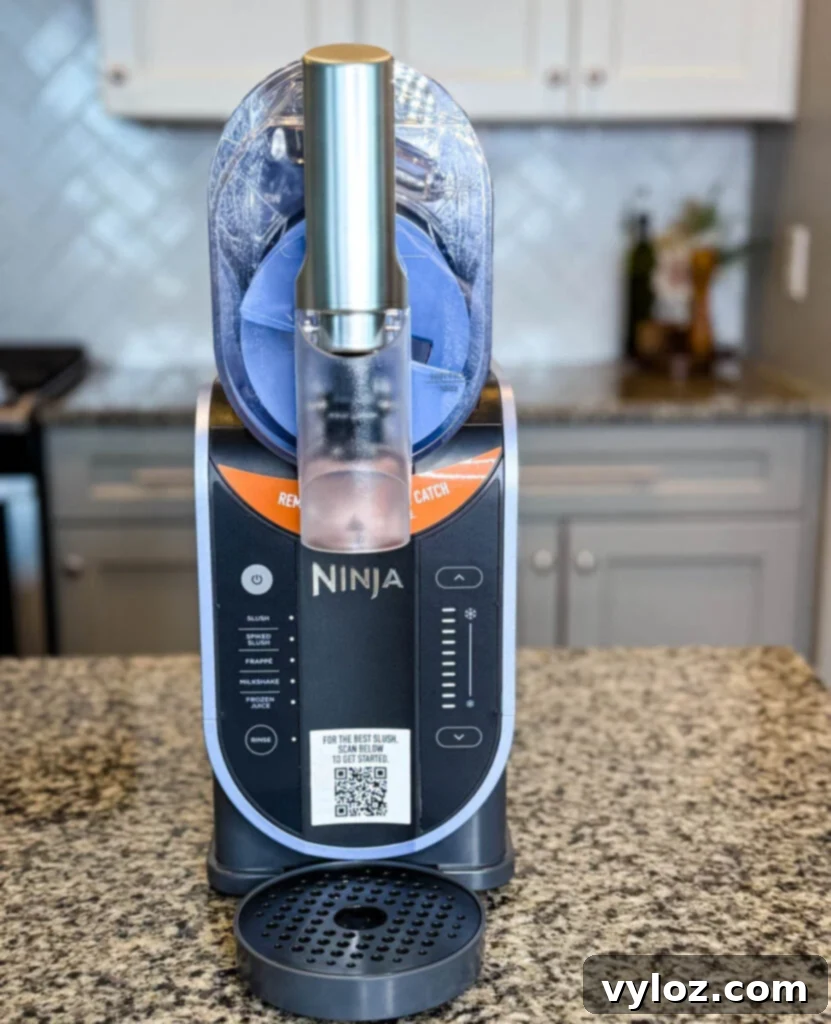 Empty Ninja SLUSHi Machine Side View – The chamber is empty, revealing the rotating auger inside. The machine is placed on a kitchen counter with a backsplash.