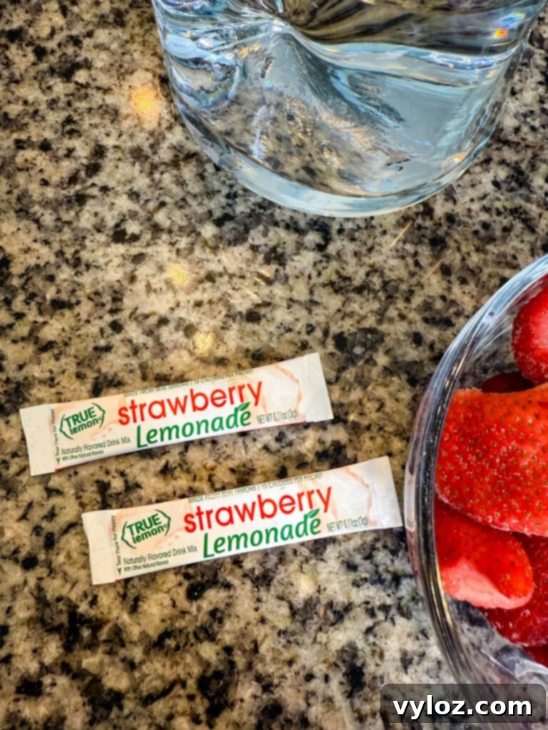 Two True Lemon Strawberry Lemonade drink mix packets on a countertop next to fresh ingredients.