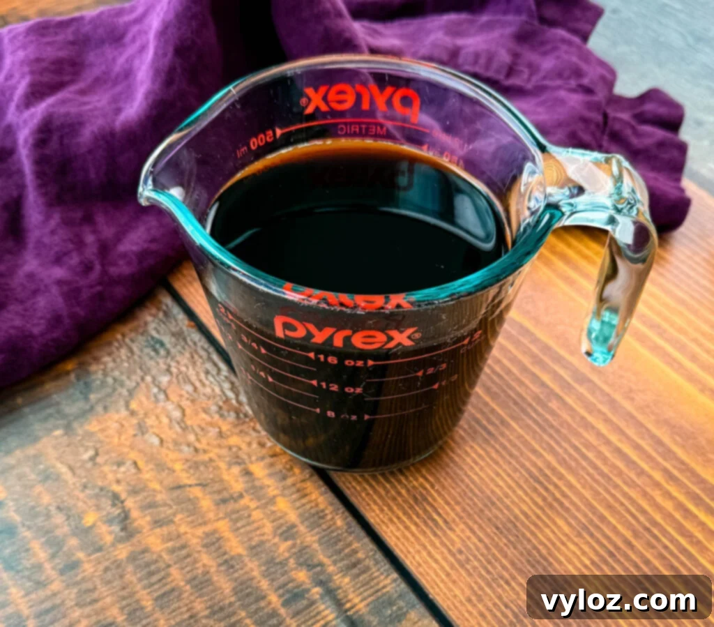 Shadow Swirl Vanilla Caramel Frappé 3 A glass Pyrex measuring cup filled with freshly brewed black coffee, sitting on a wooden table with a purple cloth partially draped behind it.