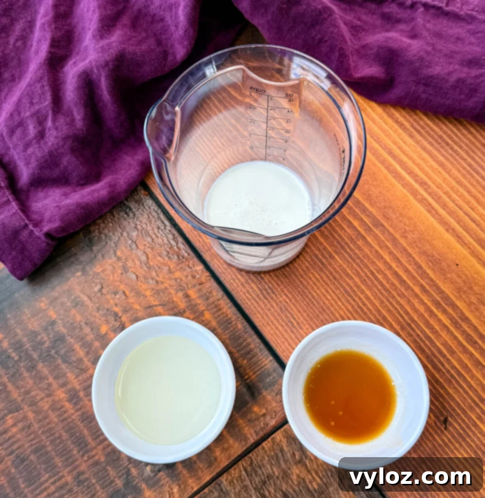 Shadow Swirl Vanilla Caramel Frappé 4 A small measuring cup containing milk and two small bowls with different liquid ingredients—one vanilla extract and sweetener—placed on a wooden table with a purple cloth in the background.