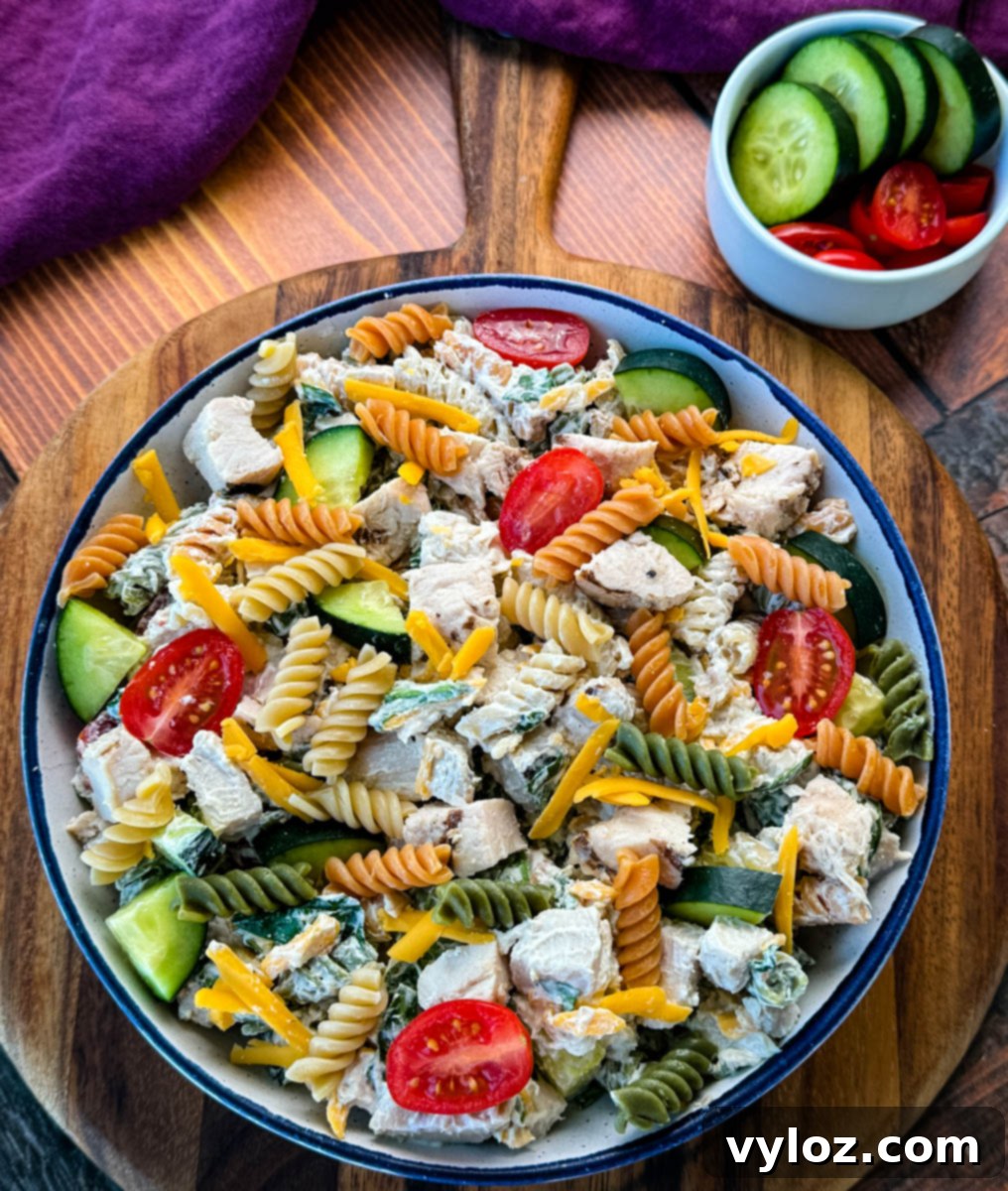 Overhead view of a vibrant High-Protein Chicken Pasta Salad served in a rustic bowl on a wooden surface, showcasing cherry tomatoes, cucumbers, and shredded cheddar cheese.