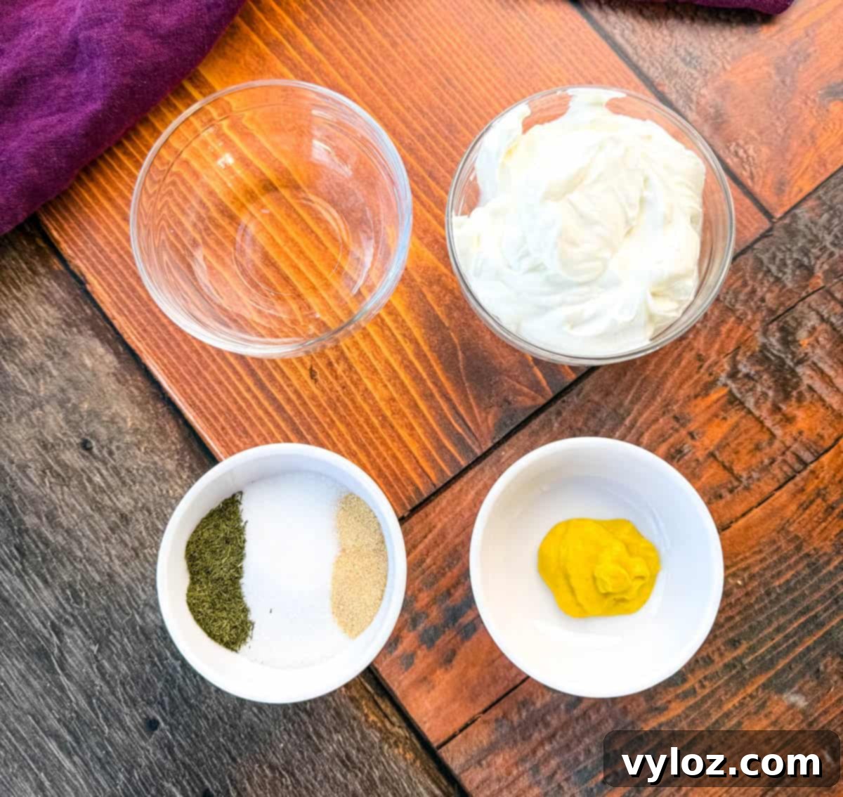 Pickle Lovers' Dream Coleslaw 3 Coleslaw Dressing Ingredients in Small Bowls – A top-down view of individual ingredients in small white bowls on a rustic wooden surface, including Greek yogurt, mustard, dried dill, sugar, garlic powder, and an empty bowl for pickle juice. A dark purple cloth is partially visible in the background.