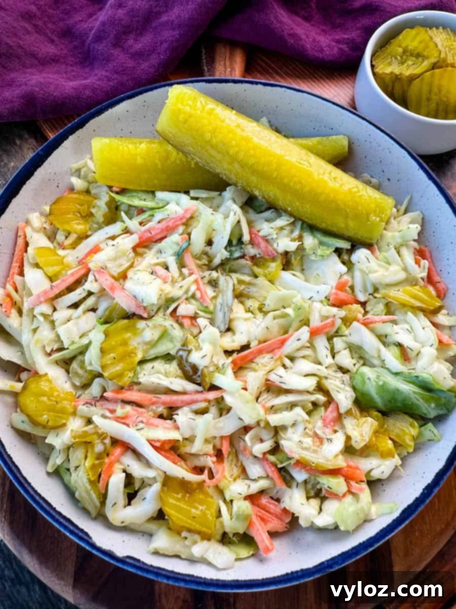 Pickle Lovers' Dream Coleslaw 7 Bowl of Dill Pickle Coleslaw with Pickle Spears on the Side – A close-up of a creamy dill pickle coleslaw served in a rustic bowl, featuring shredded cabbage, carrots, and sliced pickles, garnished with two large dill pickle spears. A small dish of extra pickle slices sits in the background on a wooden surface.