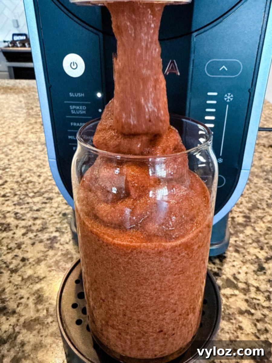 A thick, icy cherry slushi is being dispensed from the Ninja Slushi Machine into a tall glass. The texture is smooth and frosty, with the machine’s control panel visible in the background.