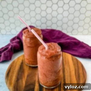 Two tall glasses filled with thick, icy cherry slushies, served with red-and-white striped straws. The drinks are placed on a round wooden serving board, with a deep purple cloth draped in the background against a white hexagonal tile backdrop.