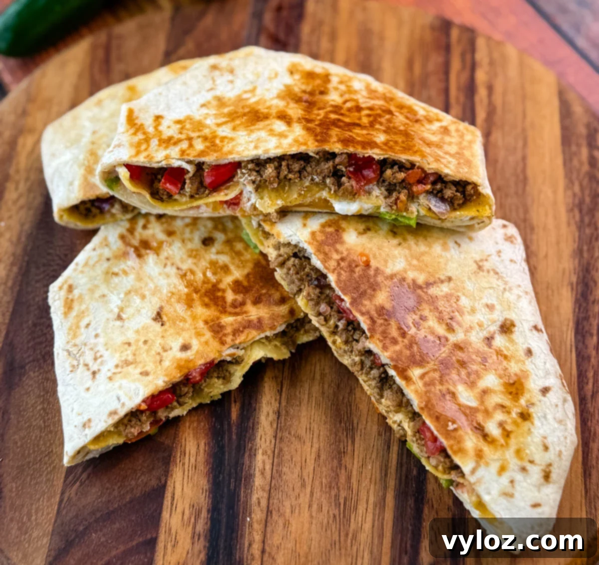 Golden brown beef and cheese crunchwrap supreme cut in half and stacked on a wooden cutting board with halved limes in the background