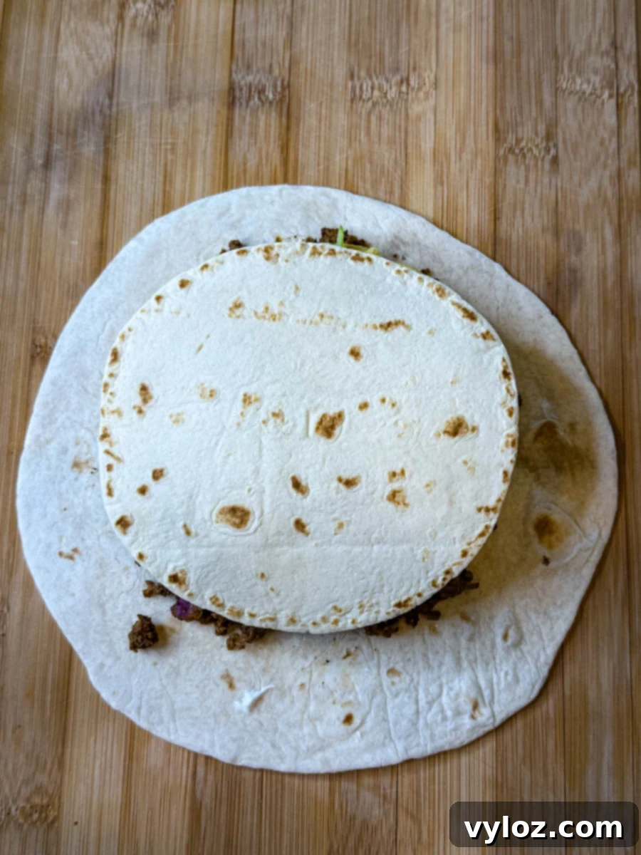 Small flour tortilla placed over the beef and cheese filling on a larger tortilla, ready to be folded into a crunchwrap.