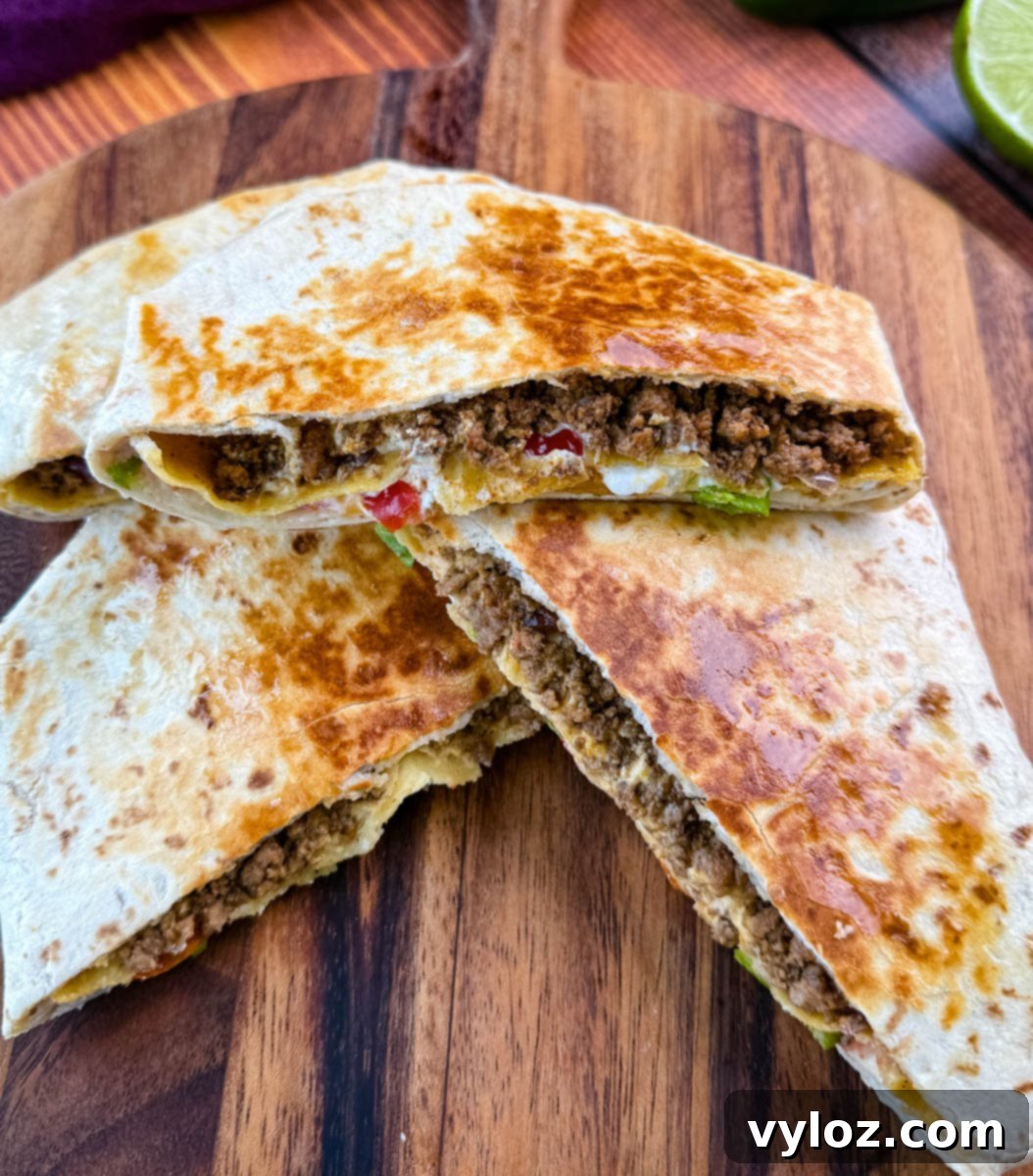 Golden brown beef and cheese crunchwrap supreme cut in half and stacked on a wooden cutting board with halved limes in the background