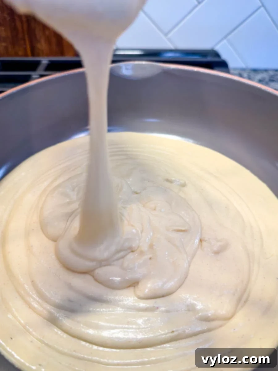 Protein-Packed Queso Dip 5 Warm, melted queso cheese dip made with cottage cheese being poured into a pot, creating thick, gooey swirls, ready to be served.