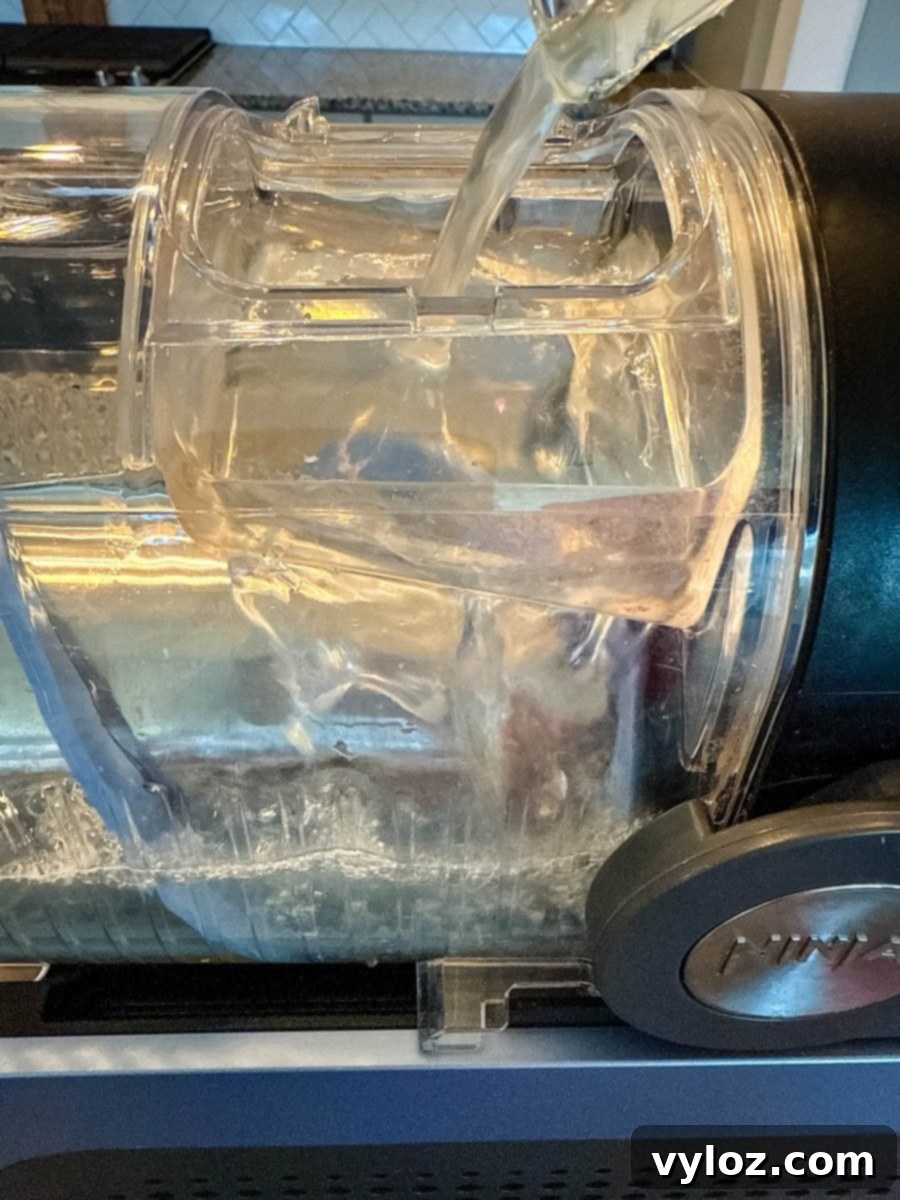 Clear liquid being poured into the top of a Ninja Slushi machine. The mixture flows into the clear canister, beginning the lemonade slush-making process.