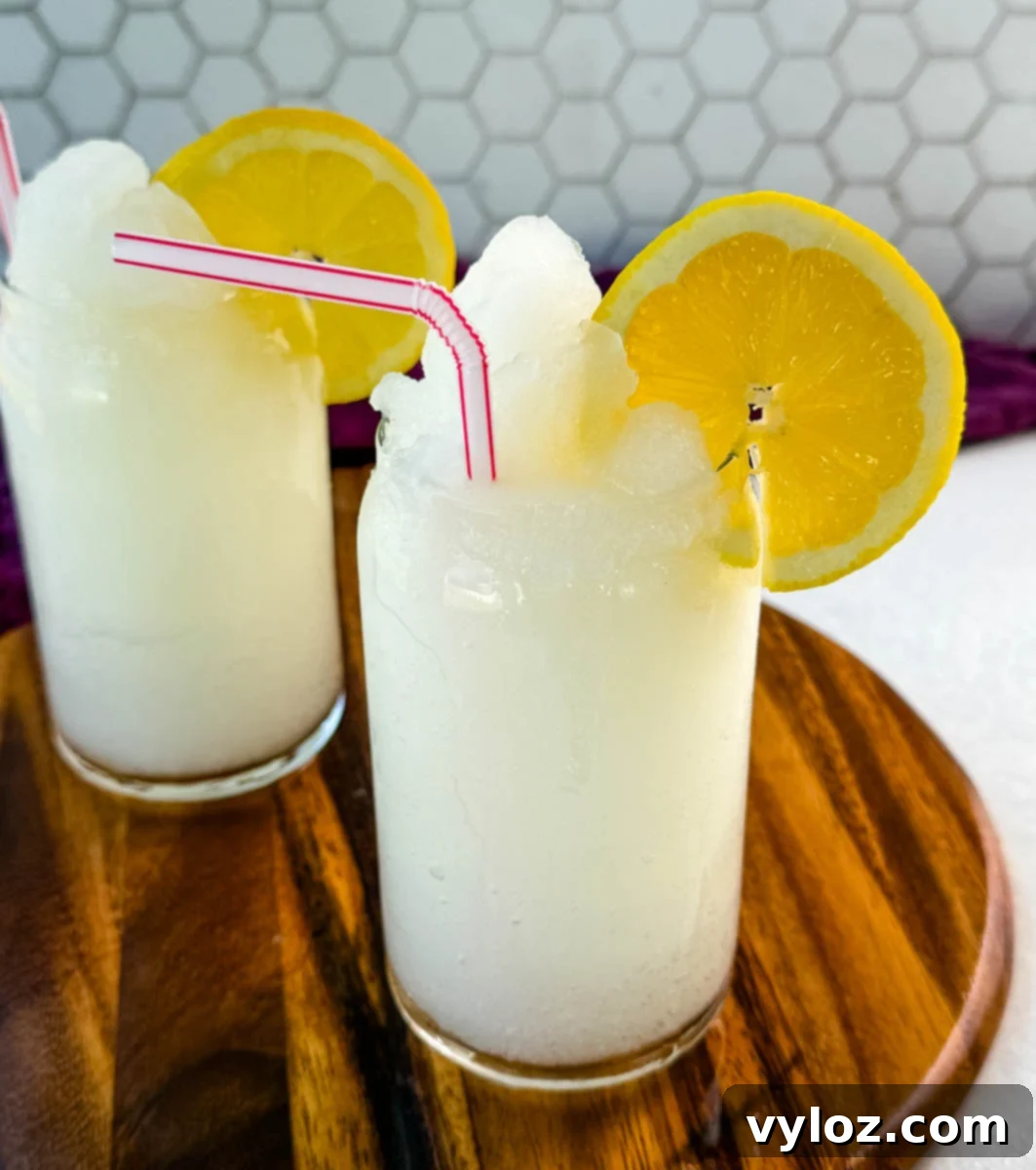 Ninja Lemon Blast 8 Two glasses of lemonade slush on a wooden board, topped with lemon slices and striped straws. A purple cloth and sliced lemons are in the background.