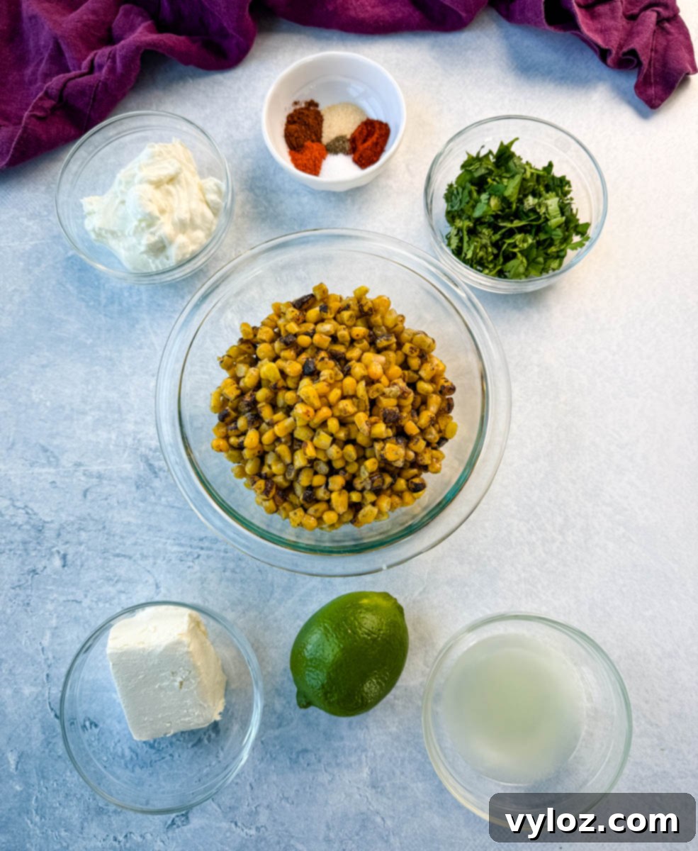 Overhead view of ingredients for street corn pasta salad: charred corn, cream cheese, sour cream, lime, lime juice, cilantro, spices, and seasonings arranged on a light surface.