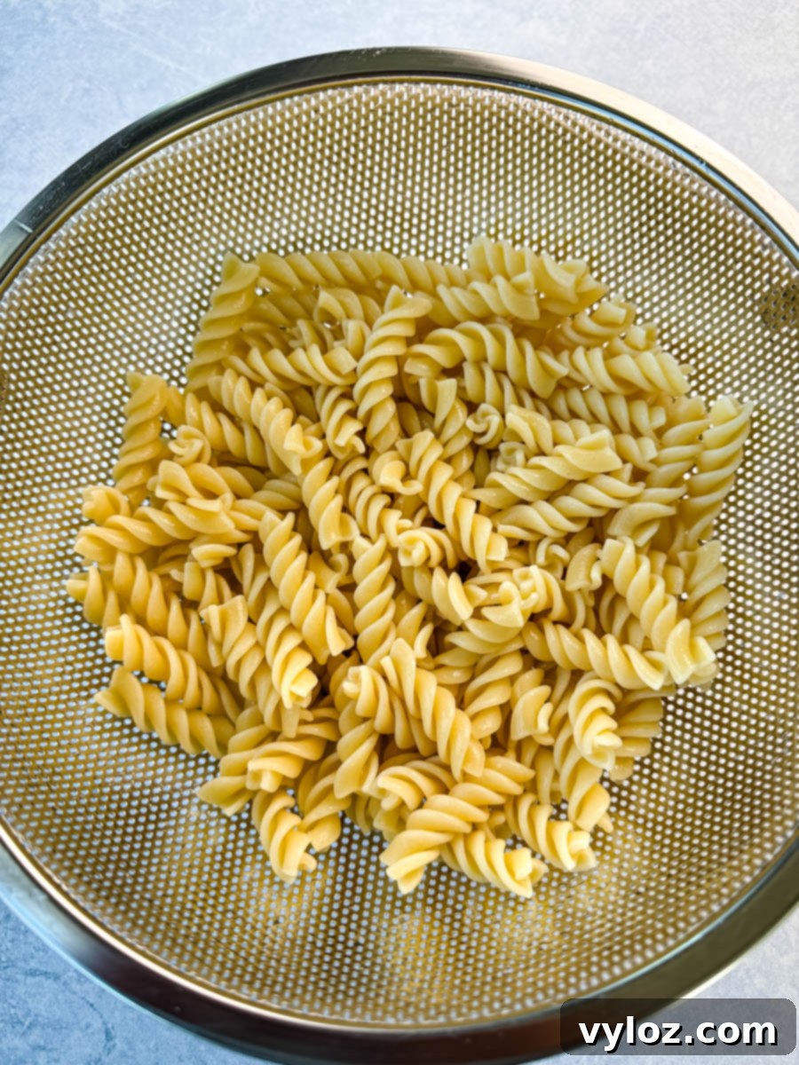 Cooked rotini pasta draining in a metal colander over a light blue surface, ready to be used in street corn pasta salad.