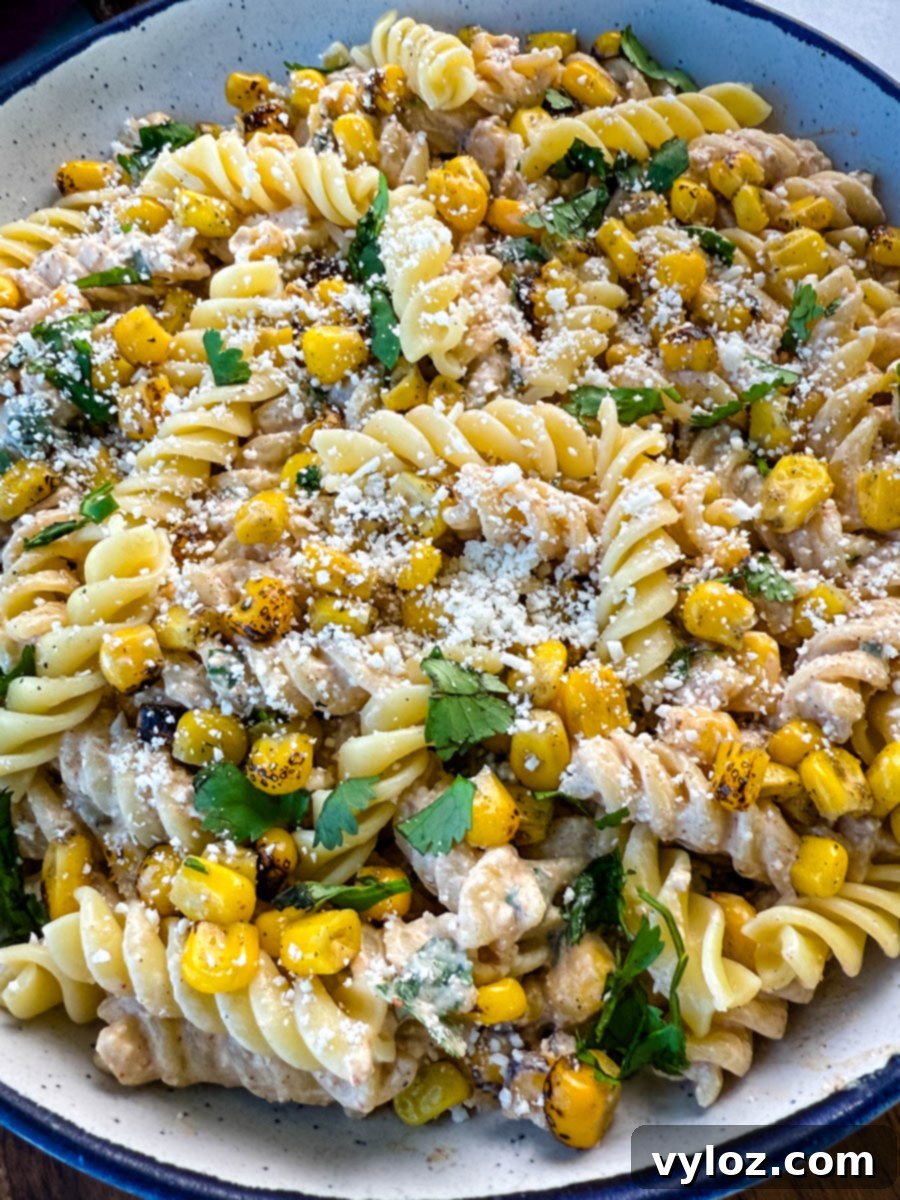 Angled close-up of street corn pasta salad showing texture of creamy dressing, grilled corn kernels, and generous cotija cheese topping.