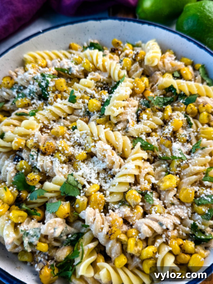 Angled close-up of street corn pasta salad showing texture of creamy dressing, grilled corn kernels, and generous cotija cheese topping.