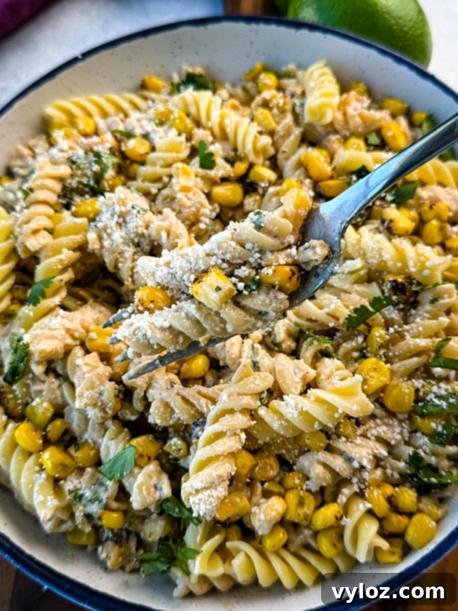 Fork lifting a bite of street corn pasta salad with charred corn, rotini pasta, cotija cheese, and fresh cilantro from a bowl.