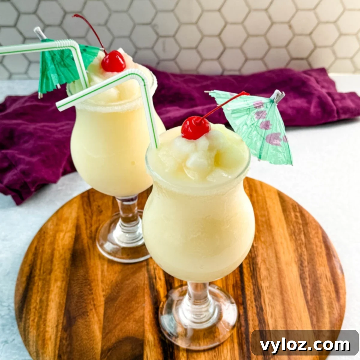 Close-up of creamy piña coladas in curved glasses with straws, cherries, and umbrellas, ready to serve.