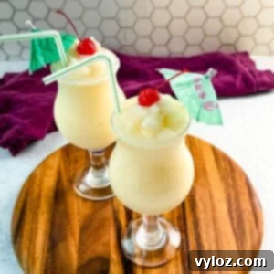 Close-up of creamy piña coladas in curved glasses with straws, cherries, and umbrellas, ready to serve.