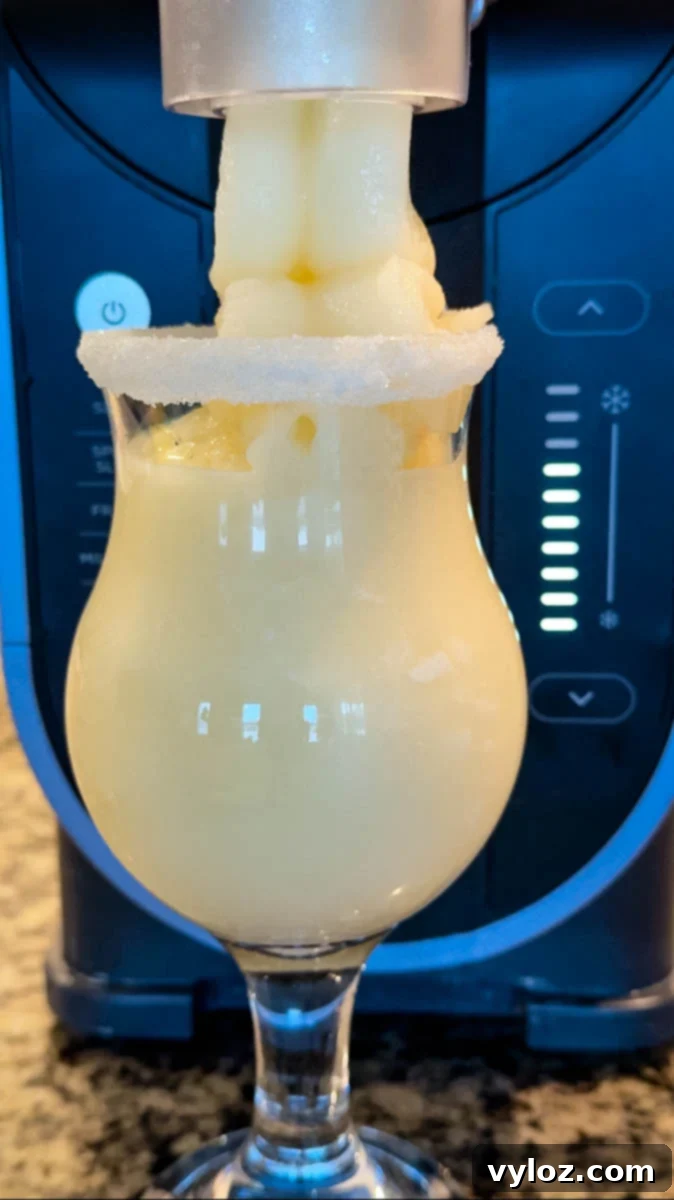 Piña colada slush dispensing from the Ninja Slushi machine into a sugar-rimmed glass.