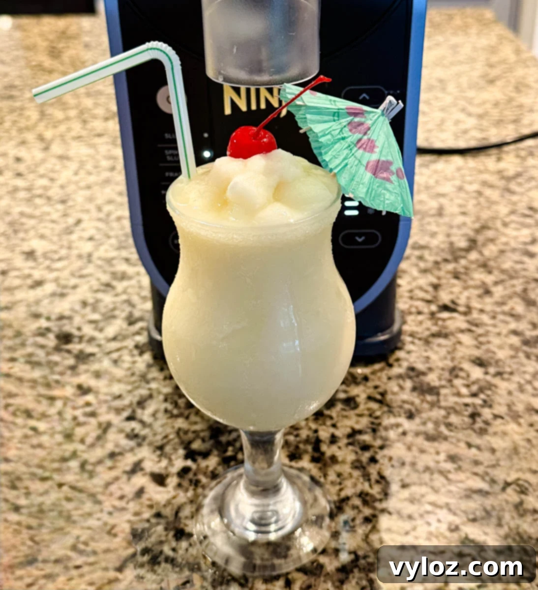 Finished piña colada dispensed into a glass directly from the Ninja Slushi machine, garnished with cherry and umbrella.