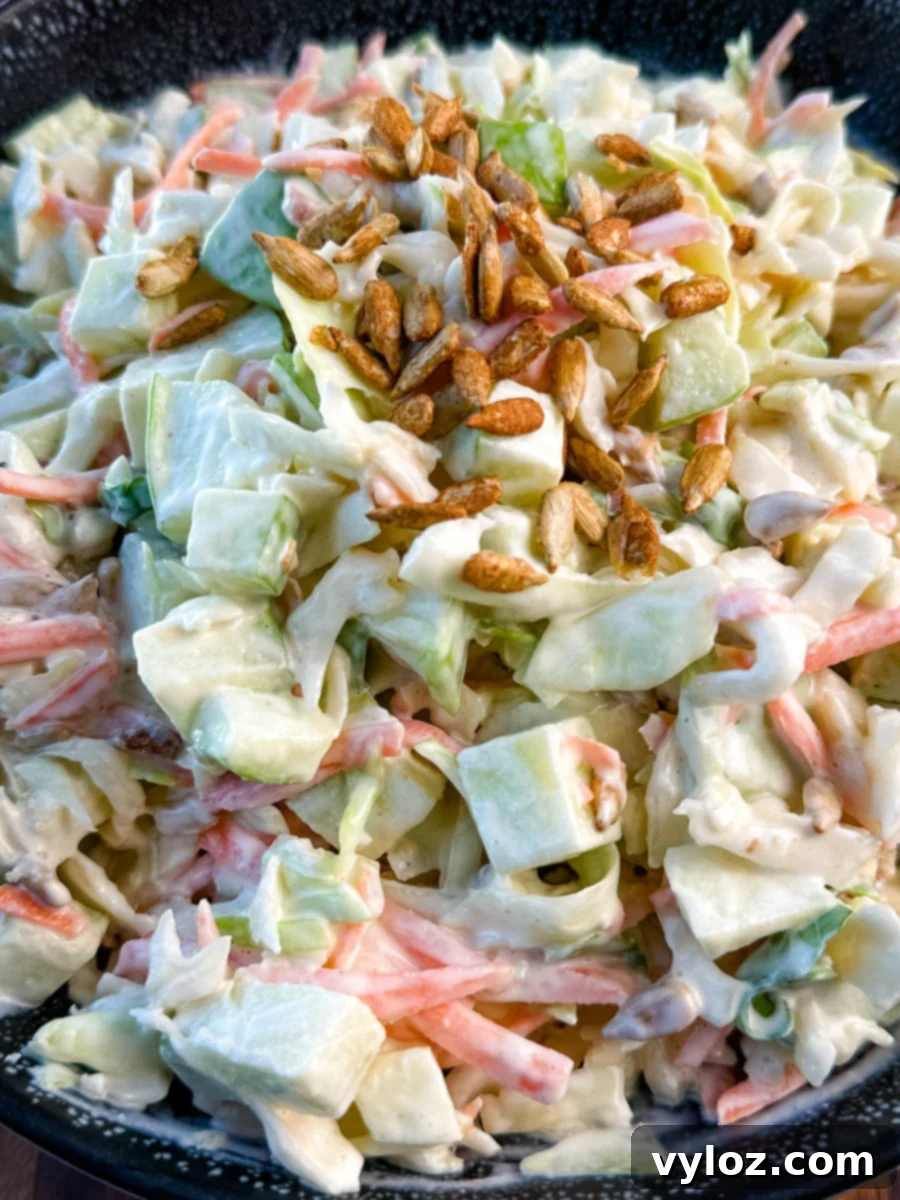 Creamy Apple Crunch Slaw 2 Close-up of creamy apple coleslaw topped with toasted sunflower seeds, showing chopped green apples, shredded cabbage, and carrots in a creamy dressing.