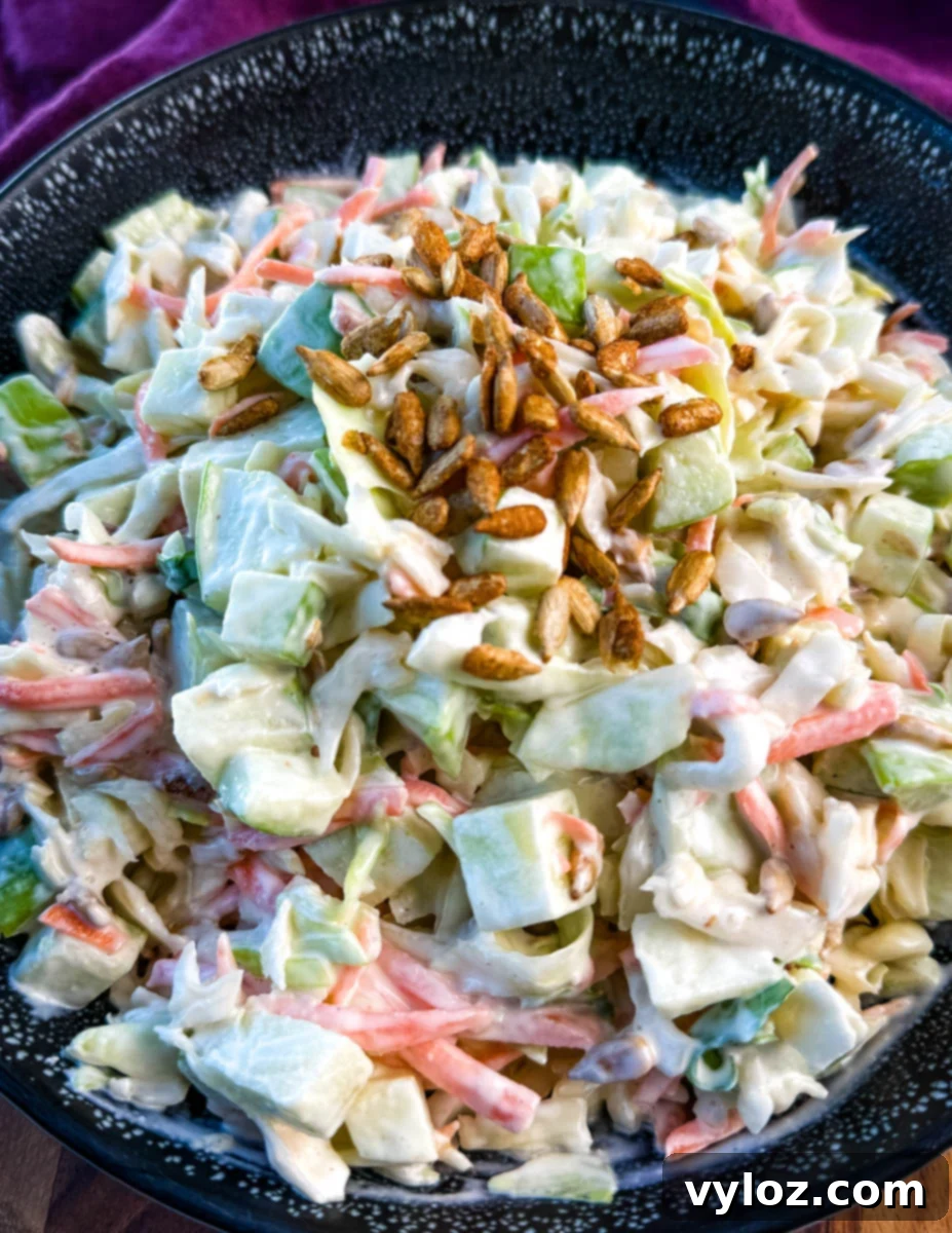 Creamy Apple Crunch Slaw 6 Close-up of creamy apple coleslaw topped with toasted sunflower seeds, showing chopped green apples, shredded cabbage, and carrots in a creamy dressing.