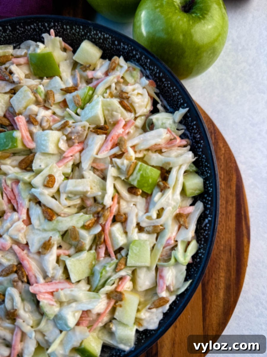 Creamy Apple Crunch Slaw 7 Overhead angle of a black speckled bowl filled with creamy apple coleslaw and sprinkled with sunflower seeds.