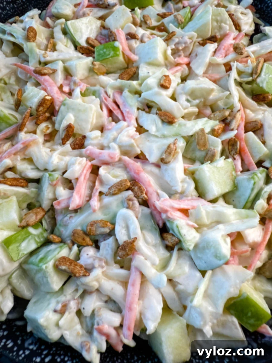 Creamy Apple Crunch Slaw 8 Close-up of creamy apple coleslaw topped with toasted sunflower seeds, showing chopped green apples, shredded cabbage, and carrots in a creamy dressing.
