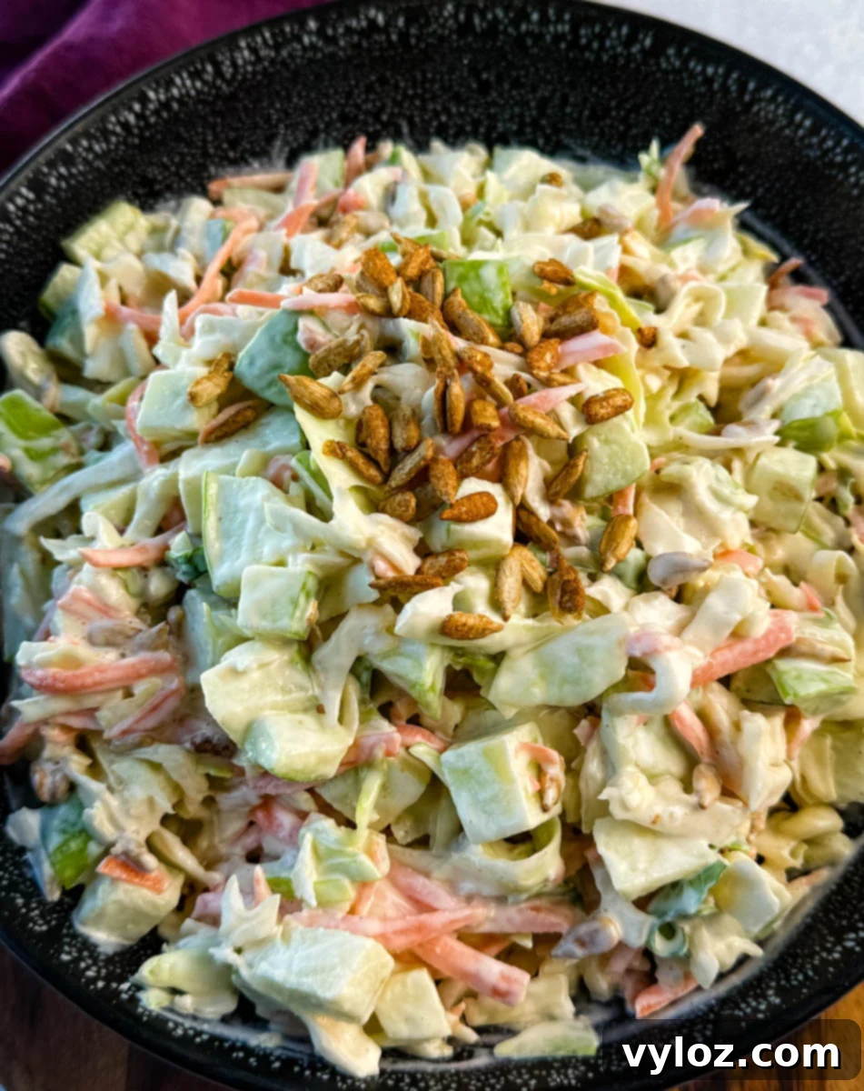 Creamy Apple Crunch Slaw 9 Close-up of creamy apple coleslaw topped with toasted sunflower seeds, showing chopped green apples, shredded cabbage, and carrots in a creamy dressing.