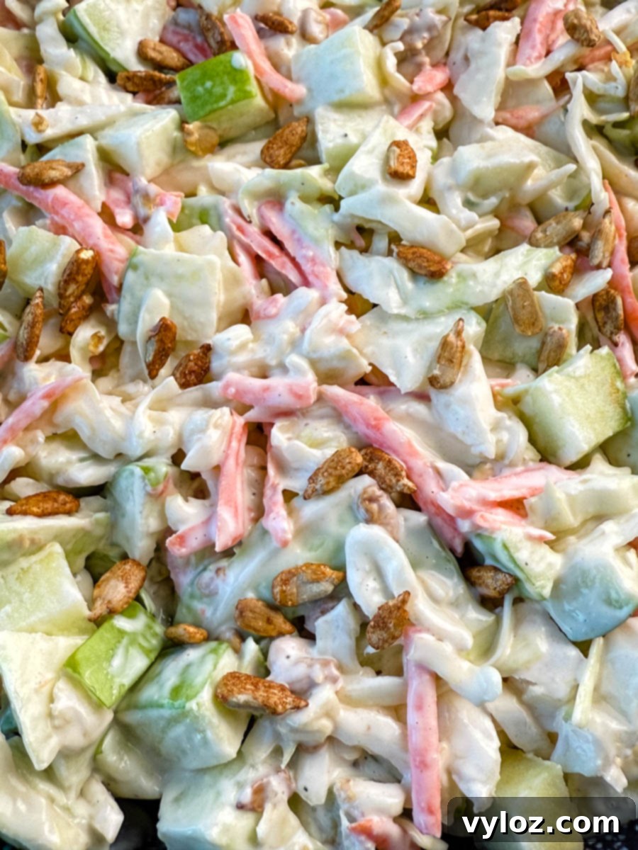 Creamy Apple Crunch Slaw 10 Close-up of creamy apple coleslaw topped with toasted sunflower seeds, showing chopped green apples, shredded cabbage, and carrots in a creamy dressing.