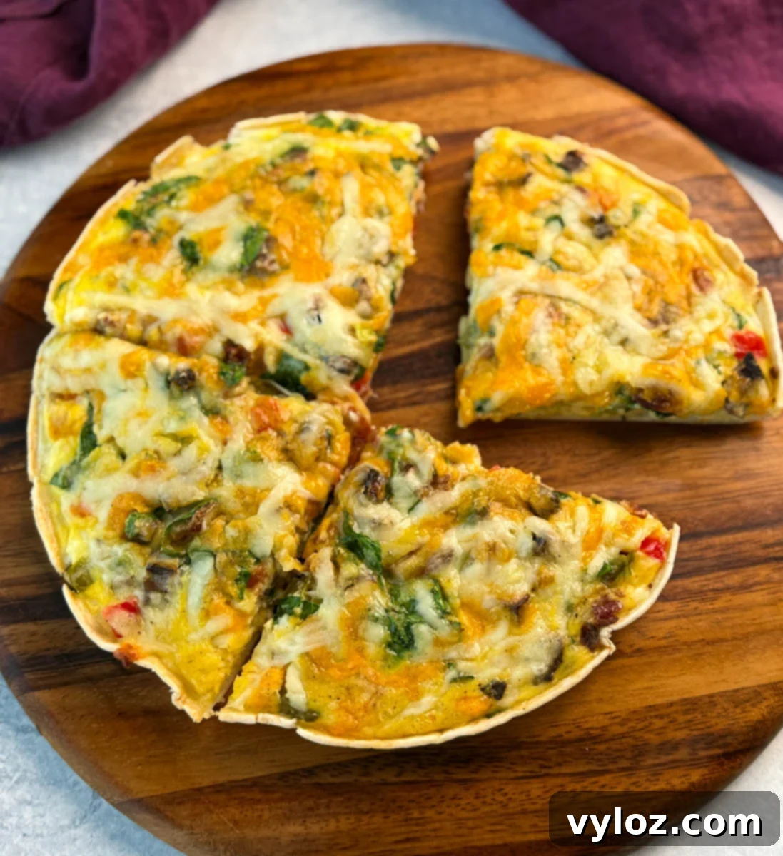 Overhead view of the full baked egg tortilla pizza sliced into four pieces, served on a round wooden board.
