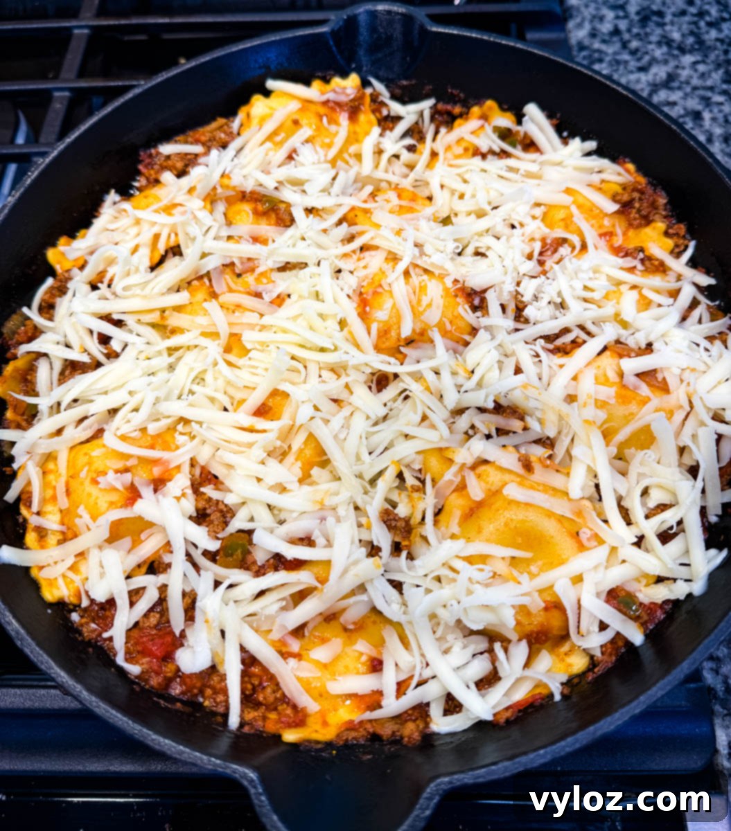 Unbaked ravioli lasagna in a cast iron skillet with shredded mozzarella cheese layered over the top, ready to be cooked.