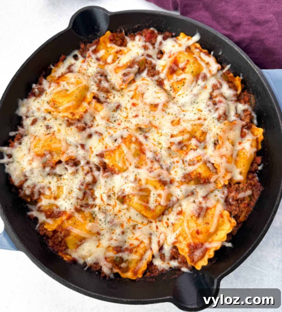 Overhead view of a finished one-pot ravioli lasagna in a cast iron skillet, topped with melted mozzarella cheese and garnished with herbs.