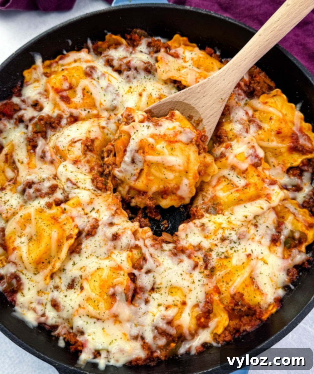 Overhead view of one-pot ravioli lasagna in a skillet, covered in melted cheese and herbs. A wooden spoon is lifting a portion from the center.