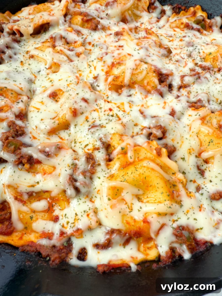 Overhead view of a finished one-pot ravioli lasagna in a cast iron skillet, topped with melted mozzarella cheese and garnished with herbs.