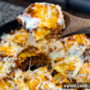 Close-up of a cheesy beef and ravioli lasagna being scooped from a cast iron skillet with a wooden spoon. Melted cheese is stretched with bits of seasoned ground beef