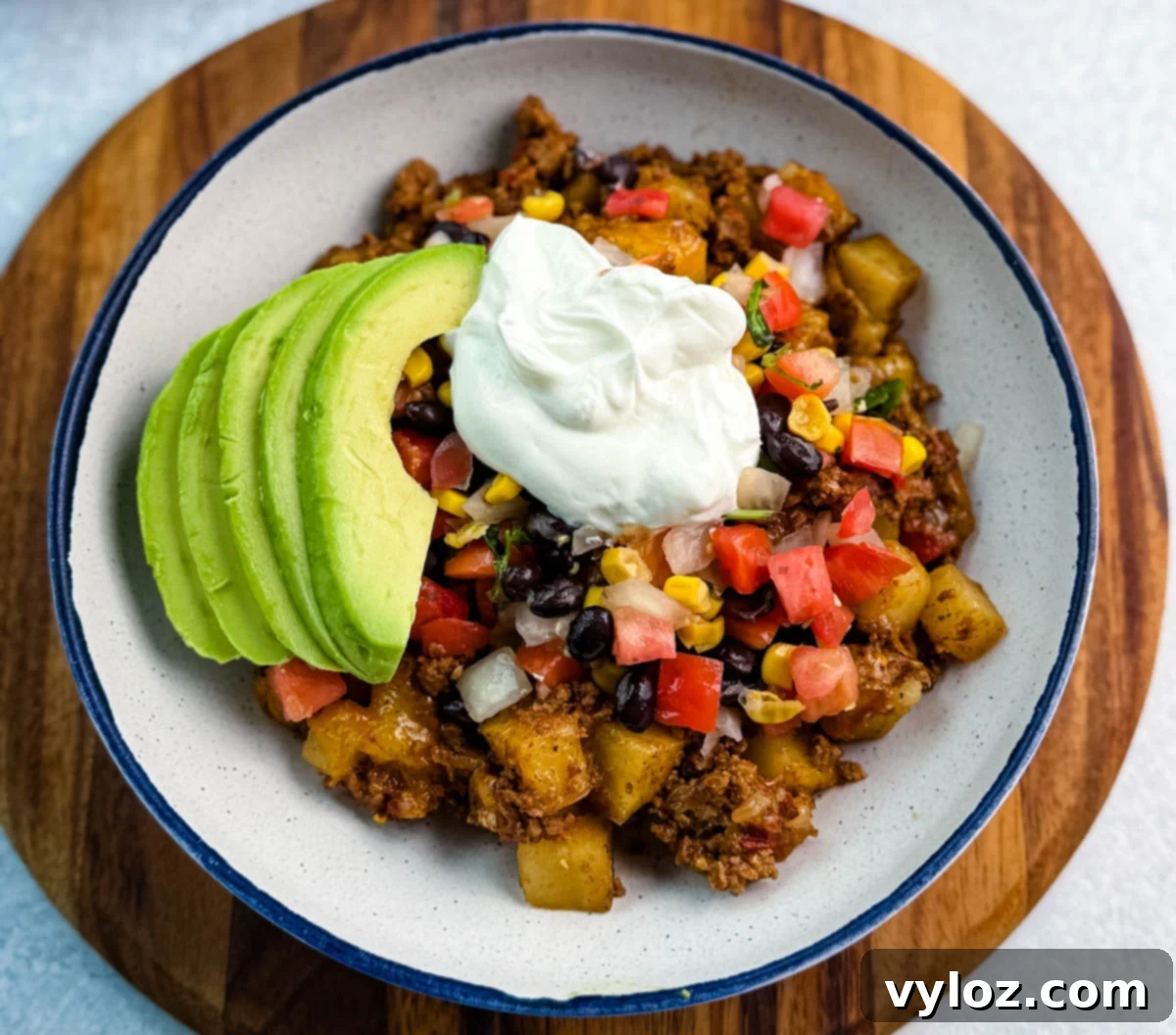 Savory Taco Potatoes 11 Center view of a hearty taco potato bowl loaded with seasoned meat, potatoes, avocado, and toppings, styled on a round white plate with a navy rim.