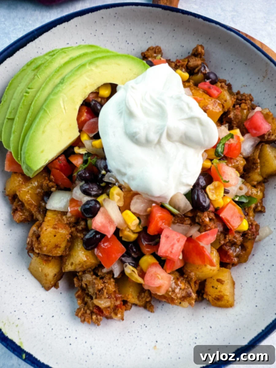 Savory Taco Potatoes 12 Bowl filled with taco-seasoned potatoes and ground meat, topped with sour cream, avocado, corn, black beans, and fresh diced veggies for a colorful, one-pot dinner.