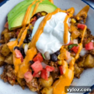 Savory Taco Potatoes 13 Bowl of loaded taco potatoes topped with avocado slices, black beans, corn, tomatoes, sour cream, and creamy orange sauce drizzle.