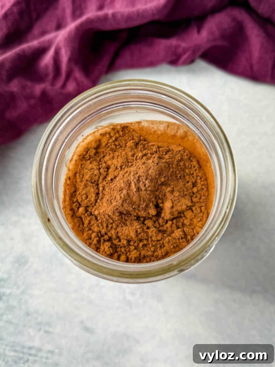 Overhead view of a small glass jar filled with unsweetened cocoa powder, set against a light surface with a deep purple cloth in the background.