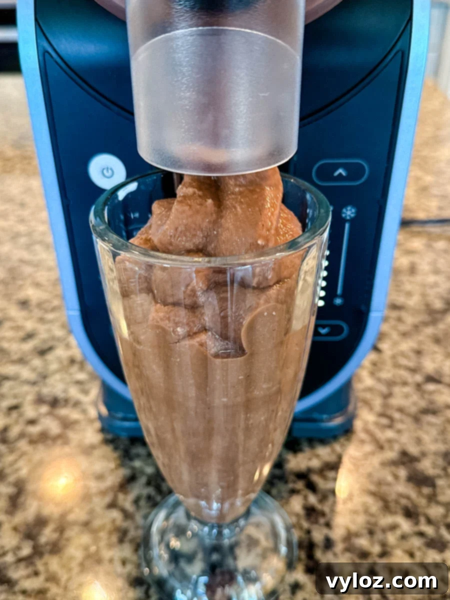 A chocolate milkshake being dispensed directly into a glass from the Ninja Slushi Machine, showcasing the smooth frozen texture and machine design.