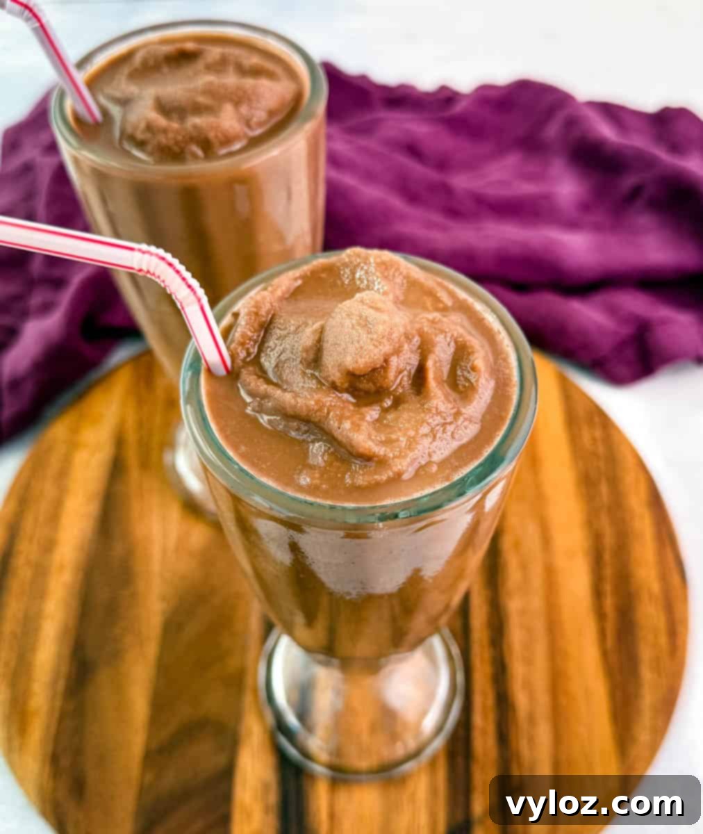 Overhead view of two chocolate milkshakes with whipped cream and red-striped straws on a wooden board, framed with a deep purple cloth.