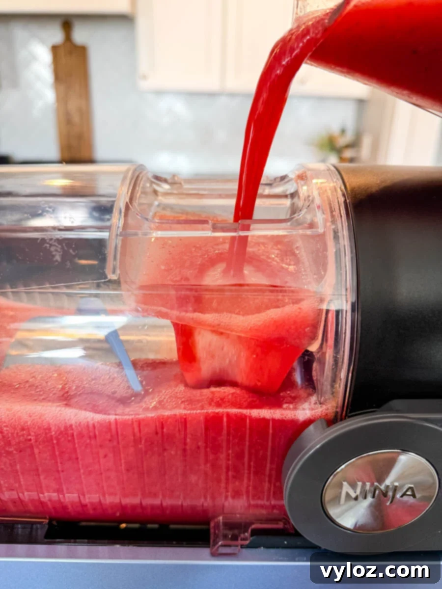 Pouring a vibrant red frosé mixture into the Ninja Slushi machine, showing the machine mid-fill with a thick, icy texture.