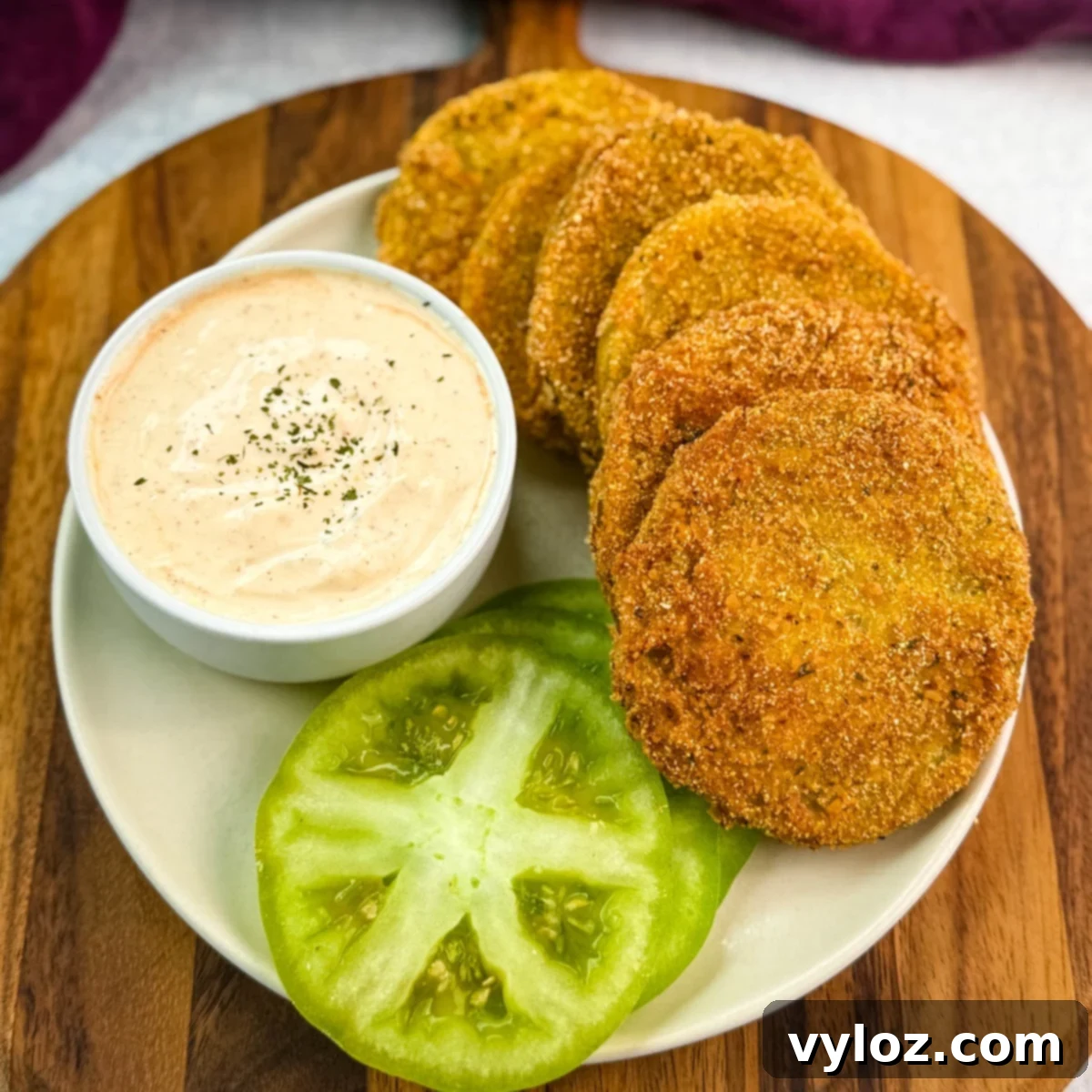 Southern Charm in Every Slice 2 Well-styled plate of crispy fried green tomatoes next to a ramekin of seasoned dipping sauce and fresh tomato slices, ideal for serving at a Southern-style meal.
