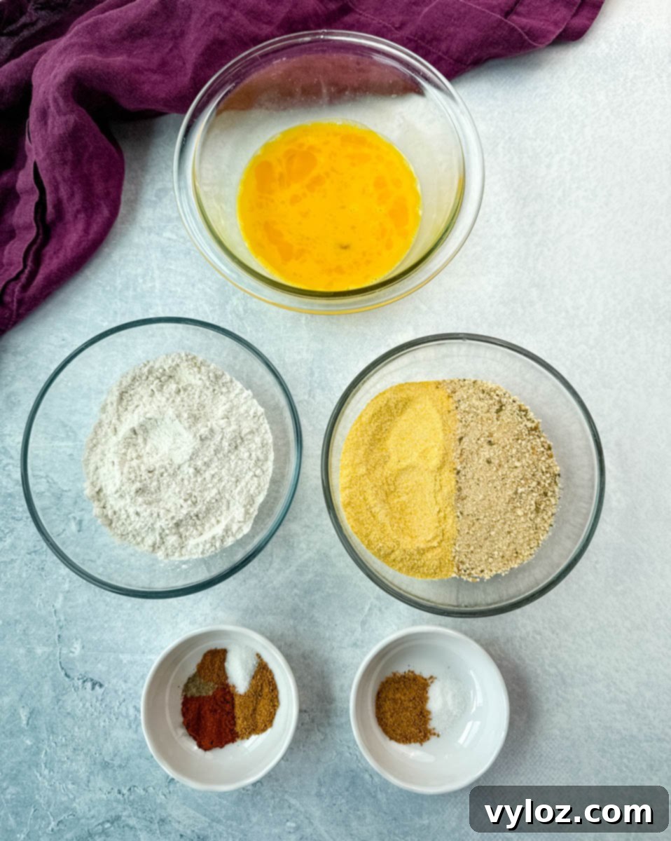 Southern Charm in Every Slice 4 Overhead shot of breading station for fried green tomatoes featuring separate bowls with beaten eggs, all-purpose flour, a mix of yellow cornmeal and breadcrumbs, and small bowls of Creole seasoning and spices.