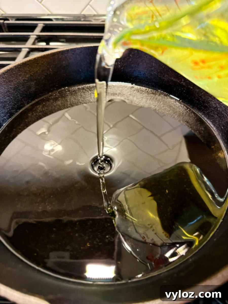 Southern Charm in Every Slice 6 Action shot of canola oil being poured into a hot cast iron skillet, preparing for frying the tomatoes.