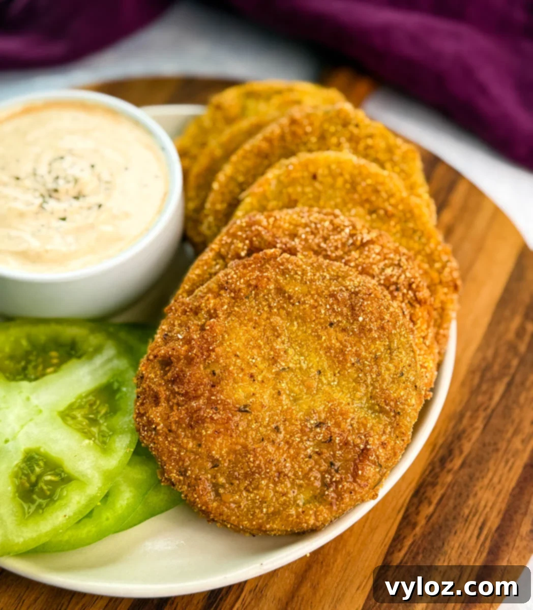 Southern Charm in Every Slice 8 Golden fried green tomatoes arranged in a fanned-out line on a plate next to a bowl of dipping sauce and fresh green tomato slices.