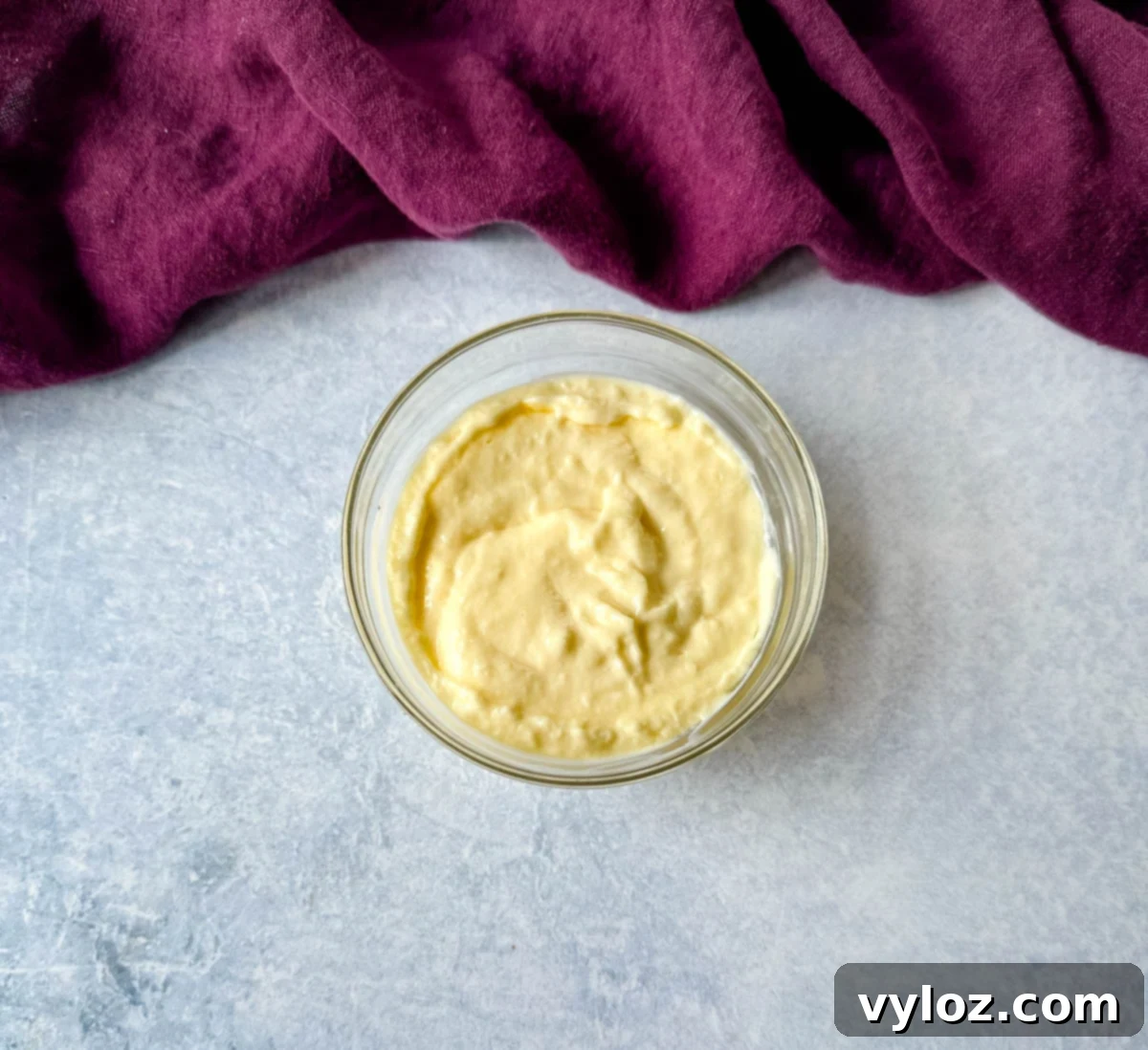 Easy Homemade Remoulade 4 Overhead shot of creamy Louisiana-style remoulade sauce in a small glass bowl on a light surface, with a deep purple kitchen towel in the background.