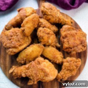 A wooden board topped with a spread of freshly fried, crispy chicken drumsticks, thighs, and wings, showcasing golden brown, crunchy coating.