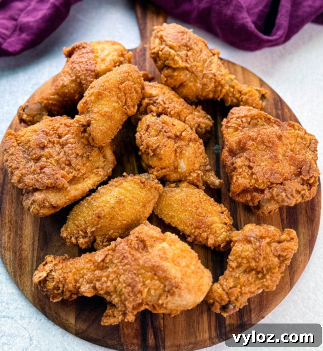 A wooden board topped with a spread of freshly fried, crispy chicken drumsticks, thighs, and wings, showcasing golden brown, crunchy coating.